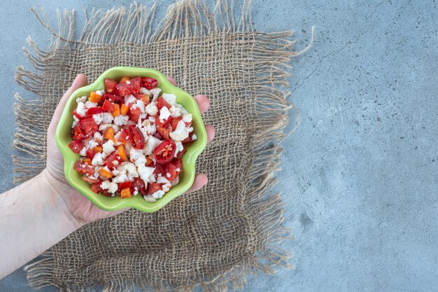 Small bowl in palm, filled with cauliflower and pepper salad on marble table.