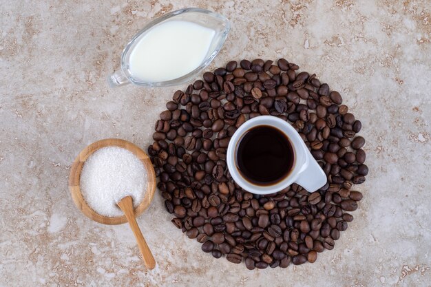 커피 한 잔을 둘러싼 커피 콩 더미 옆에 작은 설탕 그릇