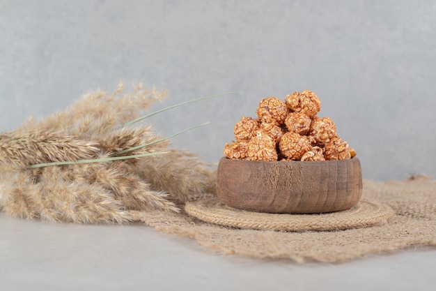 Small bowl on a trivet with a serving of popcorn candy next to stalks of needlegrass on marble table.