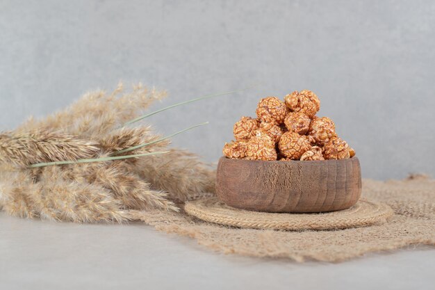 Small bowl on a trivet with a serving of popcorn candy next to stalks of needlegrass on marble table.