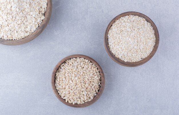 Small bowls filled with rice, oat and oat flakes on marble surface