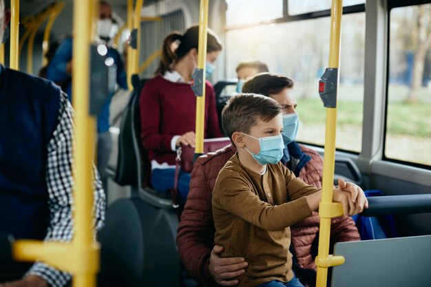 버스로 통근하는 동안 보호용 안면 마스크를 쓴 작은 소년과 아버지