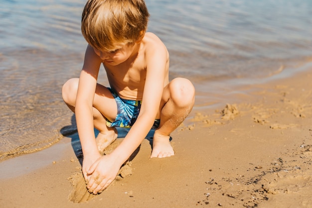 해변에서 모래를 가지고 노는 작은 소년