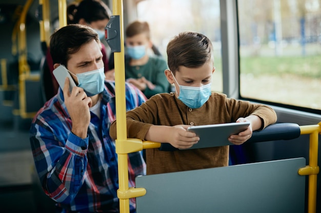 Small boy using touchpad while commuting by by with his father during coronavirus pandemic