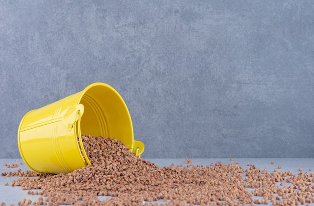 Small bucket fallen over on top of a heap of scattered buckwheat on marble surface