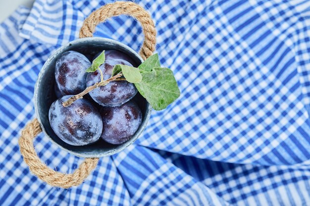 Piccolo secchio di prugne da giardino su una tovaglia blu. foto di alta qualità