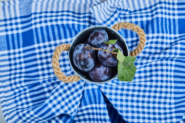 Small bucket of garden plums on a blue tablecloth. 