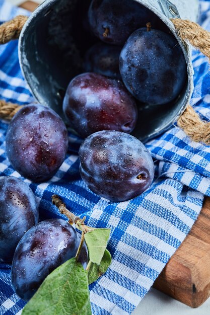 Small bucket of garden plums on blue tablecloth.