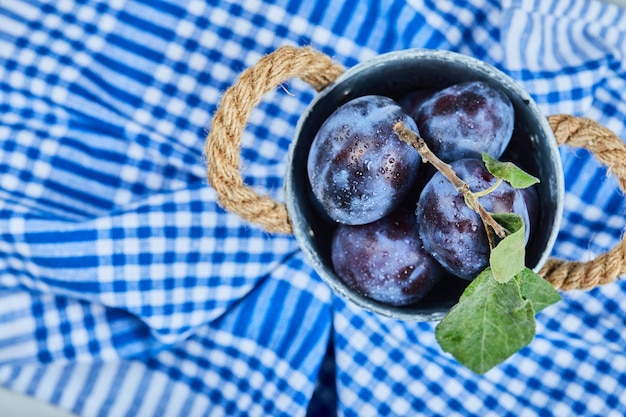 Small bucket of garden plums on blue tablecloth.