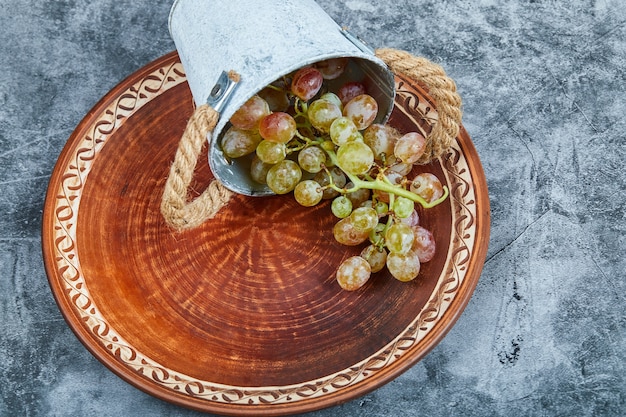 Small bucket of grapes inside ceramic plate on marble.