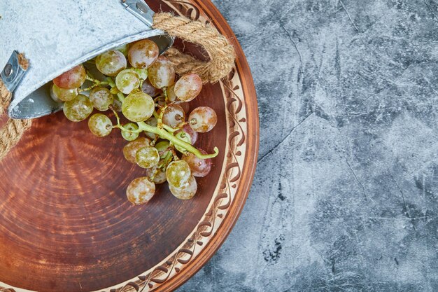 Небольшое ведерко с виноградом на керамической тарелке на мраморе.