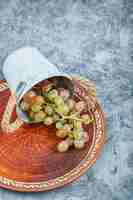 Бесплатное фото Небольшое ведро с виноградом внутри керамической тарелки на мраморном фоне. фото высокого качества