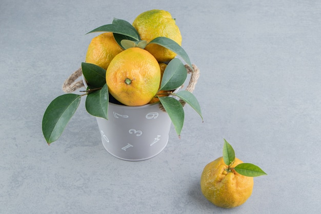 A small bucket overfilled with tangerines on marble . 