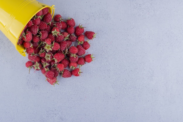 Small bucket of raspberries spilled over on marble background. High quality photo