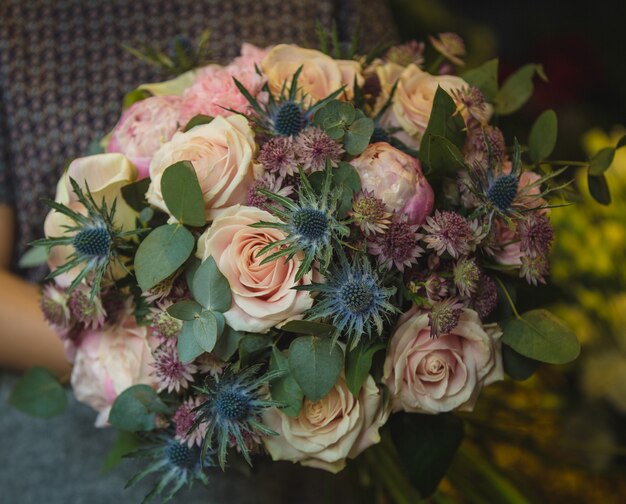 A small bunch of pink roses and decorative flowers in the hands of a woman.