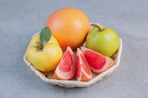 Un piccolo fascio di frutta in un cesto bianco su sfondo marmo.