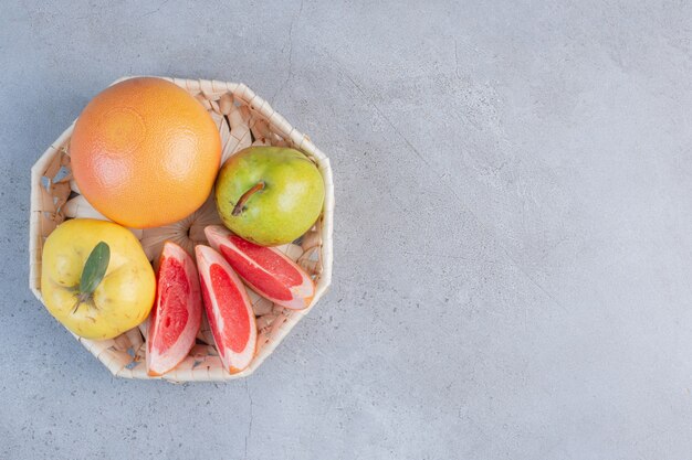 A small bundle of fruits in a white basket on marble background. 