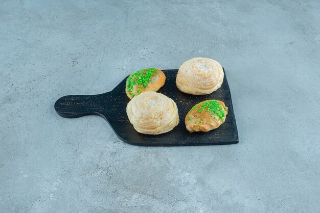 Small buns and flaky cakes on a board on marble surface