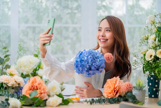 Small business Asia Female florist smile arranging flowers in floral shop Flower design store happiness smiling young lady taking photo of her vase to social media publish internet marketing ideas