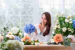 無料写真 中小企業アジア女性花屋の笑顔花屋で花をアレンジフラワーデザイン店幸せ笑顔若い女性がホームビジネスから花の仕事を準備している顧客のために花瓶を作る