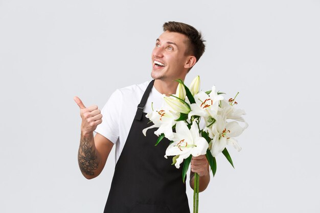 Small business retail and employees concept handsome florist salesman in flower shop pointing upper ...