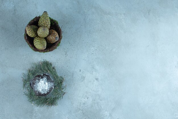 Small cake on a pile of pine leaves and a bowl of pine cones on marble.