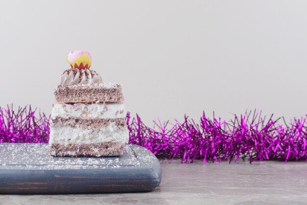 A small cake slice on a board next to a garland on marble 