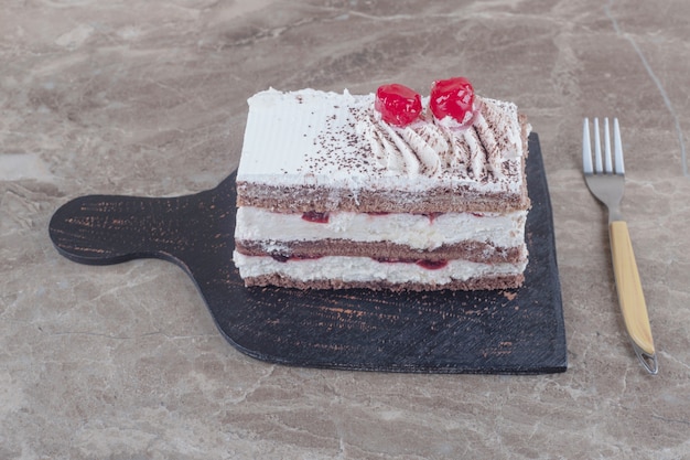 Small cake slice with cream, cherry and cocoa powder topping on a board on marble 