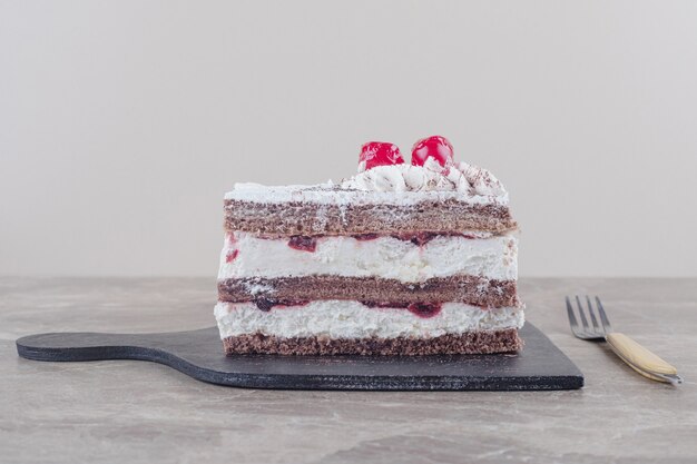 Small cake slice with cream, cherry and cocoa powder topping on a board on marble 