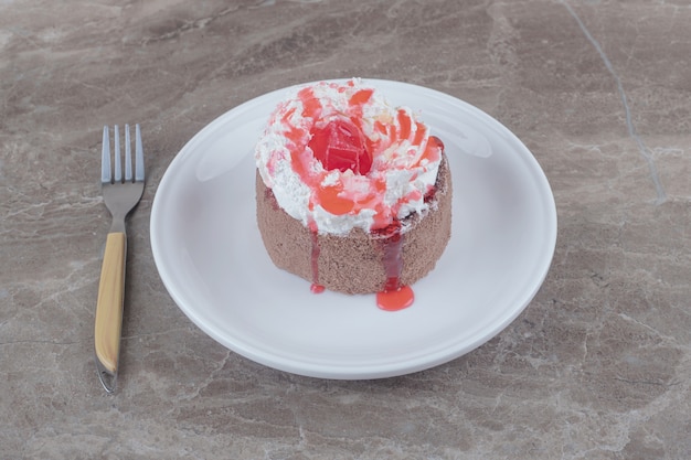 A small cake with cream and strawberry syrup topping on a plate on marble 