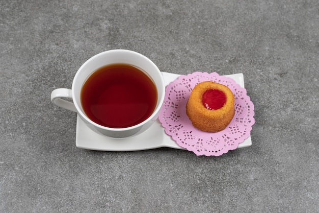 Small cake with jelly and cup of tea on marble surface