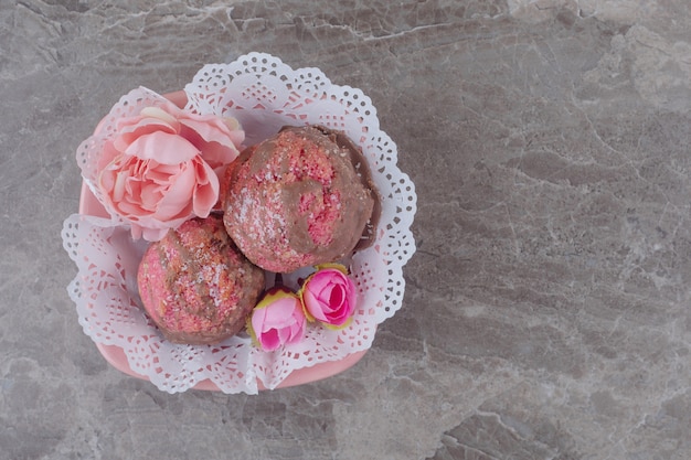 Small cakes and flower corollas in a doily-covered bowl on marble