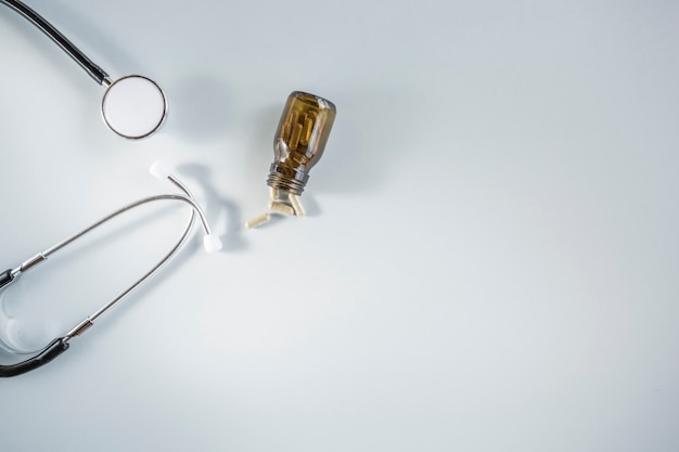 Free photo small capsule bottle fallen beside stethoscope against white background