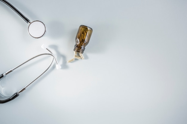 Small capsule bottle fallen beside stethoscope against white background