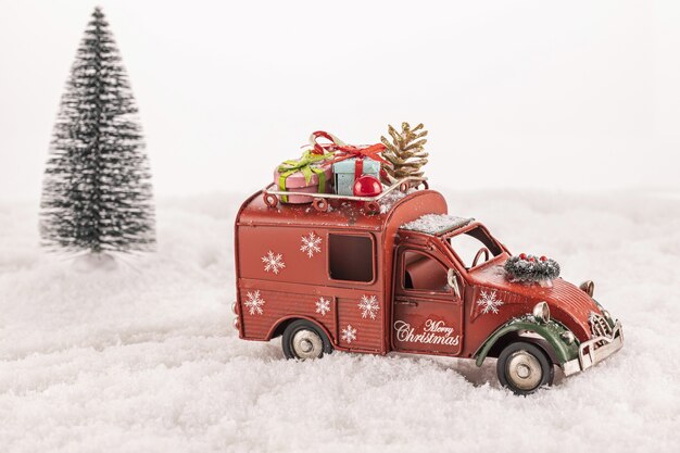 Small car toy decorated with ornaments on artificial snow with a Christmas tree in the background