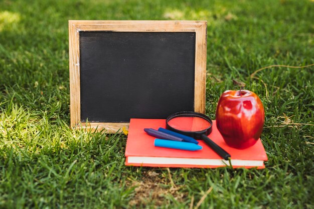 Small chalkboard and stationery with apple on grass