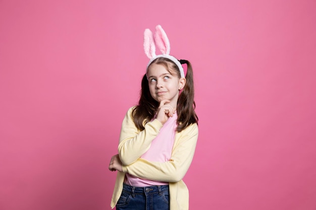 Free photo small cheerful girl acting thoughtful about easter gifts in studio