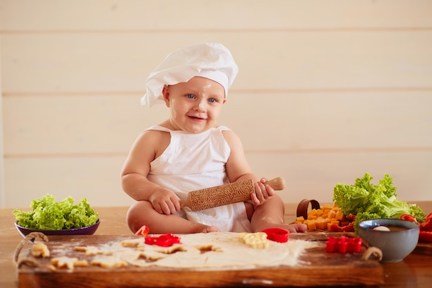 작은 아이는 반죽과 야채 근처 테이블에 앉아