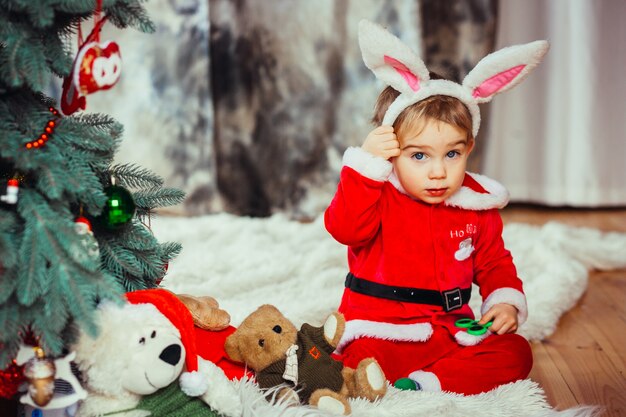 The small child sitting near Christmas tree