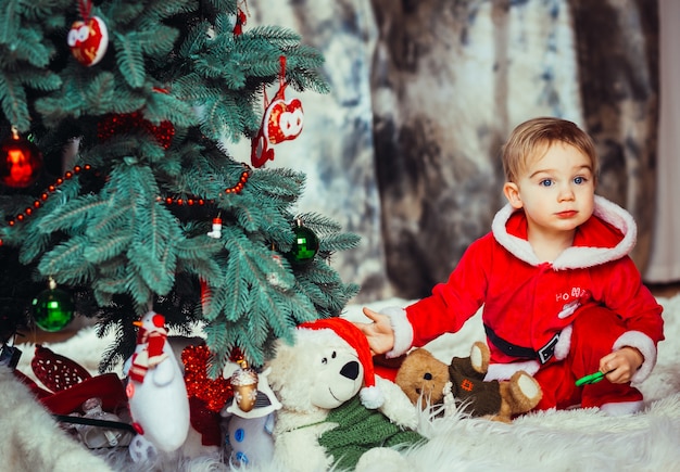 The small child sitting near Christmas tree