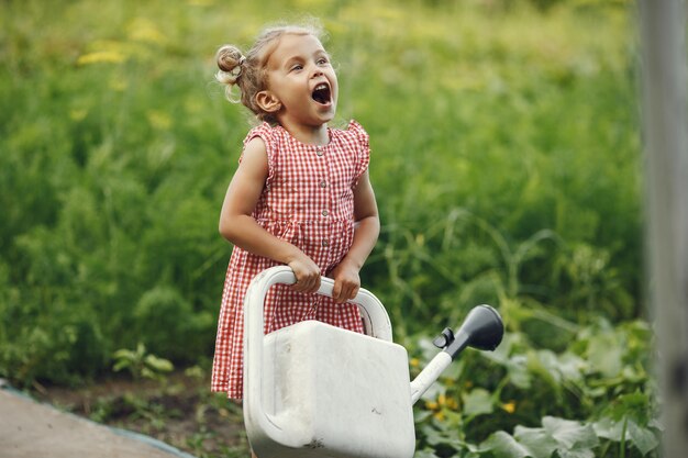 Small child with a watering can with flowers pour. Girl with a funnel. Child in a pink dress.