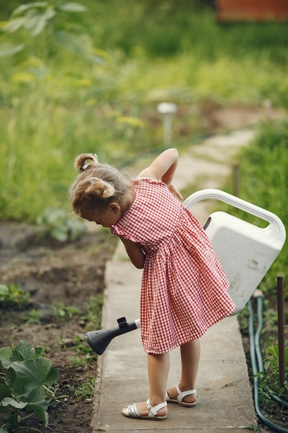 Small child with a watering can with flowers pour. Girl with a funnel. Child in a pink dress.