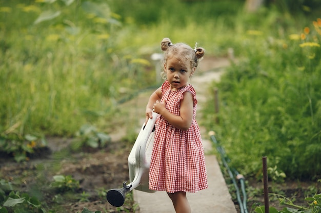Small child with a watering can with flowers pour. Girl with a funnel. Child in a pink dress.