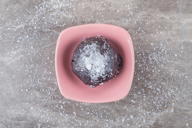 Small, chocolate coated cake in a bowl on marble surface