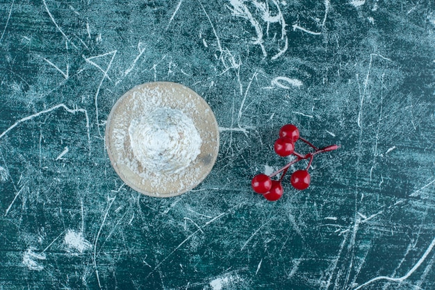 Un piccolo grappolo di bacche di natale accanto a una torta ricoperta di vaniglia sul blu.