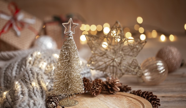 Small decorative shiny Christmas tree in close up on a blurred background of Christmas decorations, garland and bokeh lights.