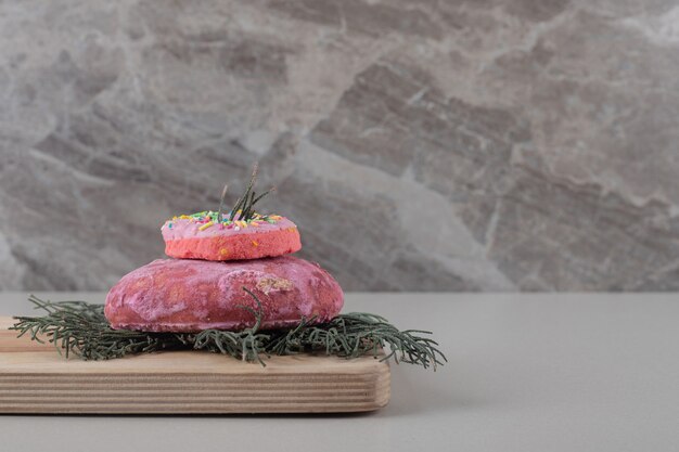 Small donut on a cookie on pine leaves on a board on marble background.