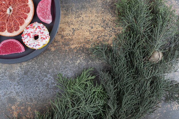 A small donut, marmelades and a grapefruit slice next to a pine branch on wooden surface