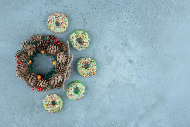 Small donuts around a pine cone wreath on marble.