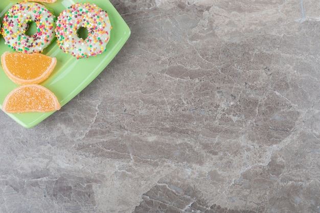 Free photo small donuts and marmelades arranged on a green platter on marble surface